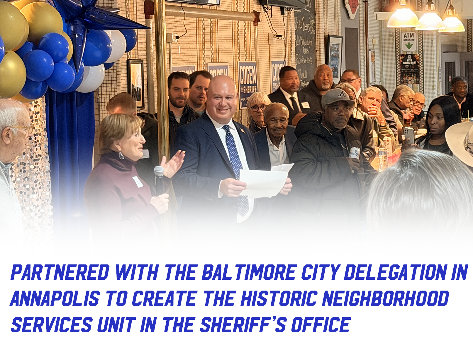 Sheriff Cogen at an event with balloons and community residents with text "Partnered with the Baltimore City Delegation in Annapolis to create the historic Neighborhood Services Unit in the Sheriff’s Office."

